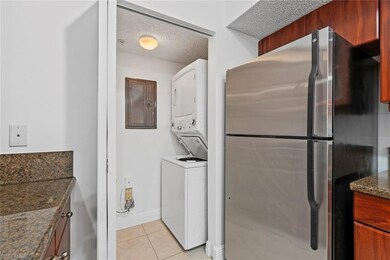 Laundry area featuring stacked washer / drying machine, light tile patterned floors, electric panel, and a textured ceiling