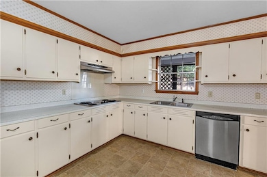 Kitchen featuring stainless steel dishwasher, light countertops, crown molding, under cabinet range hood, and tasteful backsplash