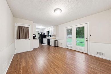 Unfurnished living room with wood finished floors, a textured ceiling, and wainscoting