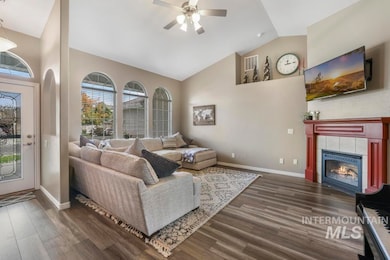 Living room featuring dark wood-style floors, a tile fireplace, ceiling fan, and high vaulted ceiling
