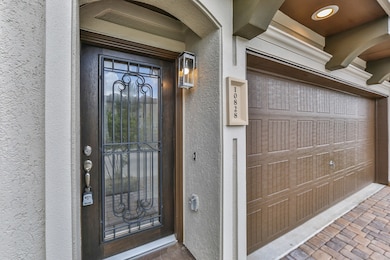 This photo shows an elegant home entrance featuring a wooden door with decorative wrought iron details and a modern lantern. Adjacent is a spacious garage with a stylish paneled door, set against a textured exterior wall.