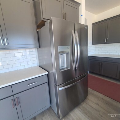 Kitchen featuring stainless steel fridge with ice dispenser, light wood-style floors, gray cabinetry, and decorative backsplash