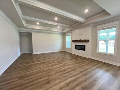 Unfurnished living room with crown molding, a tray ceiling, a fireplace, dark wood finished floors, and baseboards