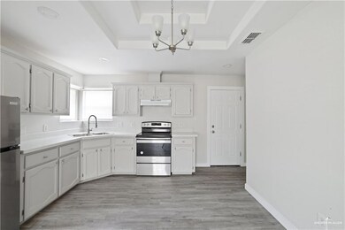 Kitchen with appliances with stainless steel finishes, a raised ceiling, under cabinet range hood, a chandelier, and light countertops