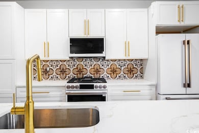 Kitchen with stainless steel gas stove, backsplash, white cabinetry, and freestanding refrigerator