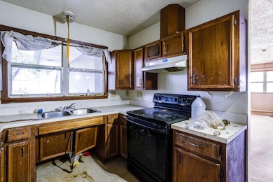 Kitchen with a textured ceiling, electric range, under cabinet range hood, and light countertops
