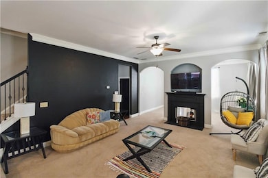Carpeted living room with arched walkways, ornamental molding, and a ceiling fan