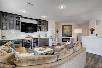 Indoor dry bar featuring glass insert cabinets, beverage cooler, decorative backsplash, dark wood finished floors, and recessed lighting