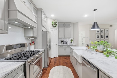 Kitchen featuring appliances with stainless steel finishes, dark wood-style floors, premium range hood, pendant lighting, and gray cabinetry