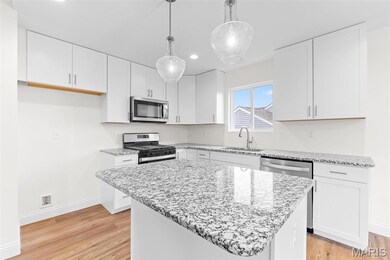 Kitchen with appliances with stainless steel finishes, light stone counters, light wood-style flooring, decorative light fixtures, and white cabinetry