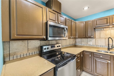 Kitchen featuring appliances with stainless steel finishes, decorative backsplash, and light stone counters