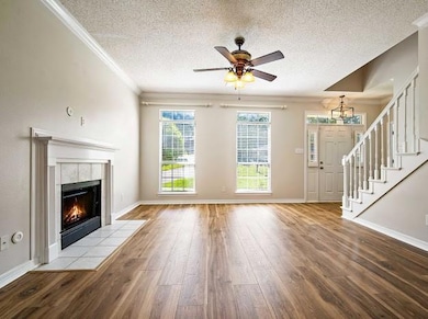 Unfurnished living room with wood finished floors, crown molding, a tiled fireplace, a textured ceiling, and ceiling fan