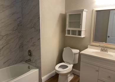 Bathroom featuring bathtub / shower combination, baseboards, vanity, and a textured wall