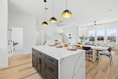 Open-concept living with a statement waterfall island, black lower cabinets, modern pendant lights, and seamless flow to dining and living spaces.