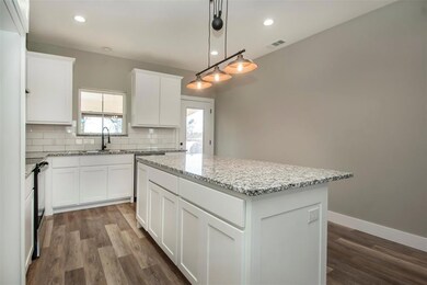Kitchen with white cabinetry, a center island, sink, light stone counters, and backsplash