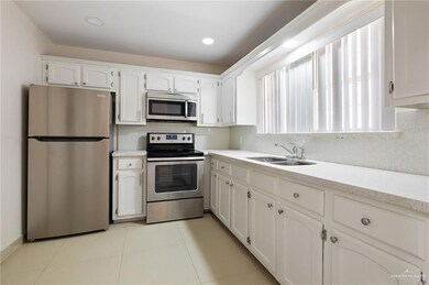 Kitchen featuring tasteful backsplash, light tile patterned floors, appliances with stainless steel finishes, white cabinets, and a sink