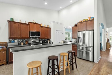 Kitchen featuring stainless steel appliances, a towering ceiling, a kitchen island with sink, a breakfast bar, and decorative backsplash