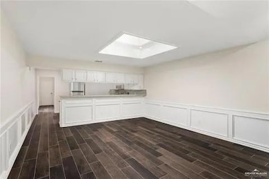 Kitchen with a skylight, a decorative wall, white cabinetry, dark wood finished floors, and a wainscoted wall