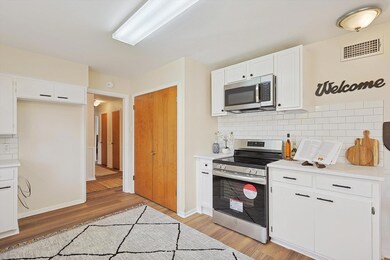 Kitchen featuring backsplash, appliances with stainless steel finishes, light hardwood / wood-style flooring, and white cabinets