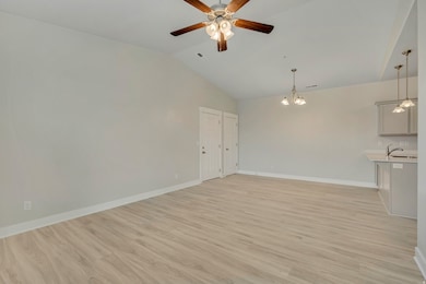 Unfurnished living room with light wood-style floors, lofted ceiling, a chandelier, and a ceiling fan