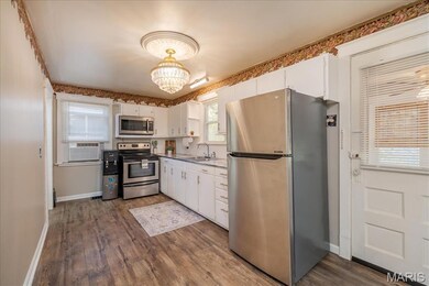 Main floor Kitchen featuring appliances with stainless steel finishes, white cabinets, a chandelier, dark wood-type flooring, and light countertops