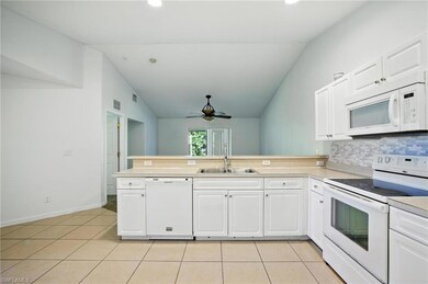 Kitchen featuring white appliances, a peninsula, vaulted ceiling, light tile patterned floors, and light countertops