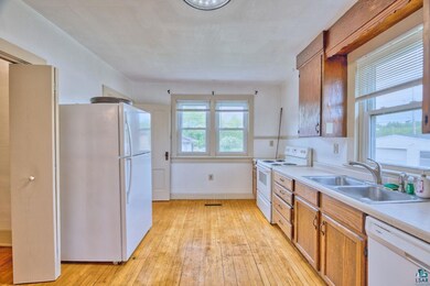 Kitchen with white appliances, a sink, light wood-style floors, light countertops, and brown cabinetry