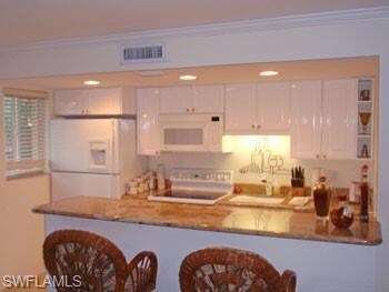 Kitchen featuring white cabinets, a kitchen breakfast bar, ornamental molding, white appliances, and a peninsula
