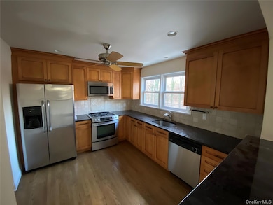 Kitchen with stainless steel appliances, decorative backsplash, dark stone countertops, light wood-type flooring, and a ceiling fan