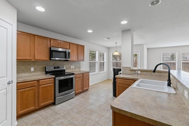 Kitchen with stainless steel appliances, brown cabinetry, light countertops, pendant lighting, and light tile patterned floors