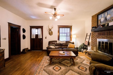 Living room with a ceiling fan, wood finished floors, a brick fireplace, and a textured ceiling