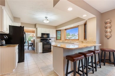 Kitchen with a peninsula, black appliances, light stone counters, a kitchen breakfast bar, and recessed lighting