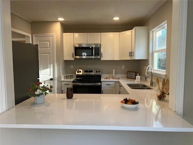 Kitchen with sink, white cabinetry, stainless steel appliances, ornamental molding, and kitchen peninsula