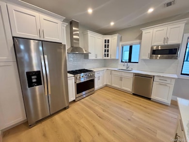 Kitchen with stainless steel appliances, wall chimney range hood, white cabinets, and recessed lighting