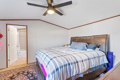 Bedroom featuring ornamental molding, lofted ceiling, light stone finish floors, ceiling fan, and ensuite bath