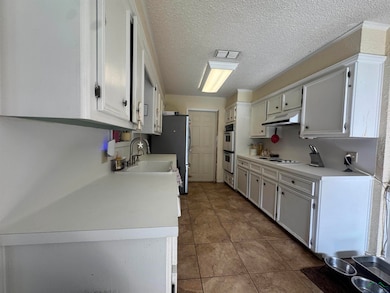 Kitchen with light countertops, freestanding refrigerator, tile patterned floors, white cabinetry, and a textured ceiling