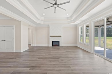 Unfurnished living room with ceiling fan, a tray ceiling, wood finished floors, a large fireplace, and crown molding