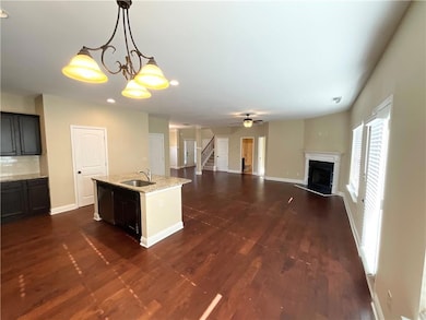 Kitchen with a fireplace, decorative backsplash, light stone counters, dark wood-style flooring, and an island with sink