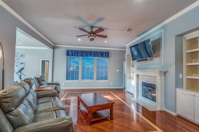 Living room with ornamental molding, built in features, ceiling fan, wood finished floors, and a tile fireplace
