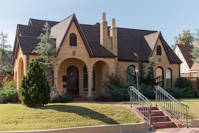 Tudor-style house featuring a front lawn, a shingled roof, brick siding, covered porch, and a chimney