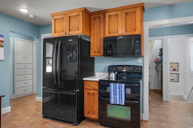 Kitchen with black appliances, brown cabinetry, light countertops, and a textured ceiling