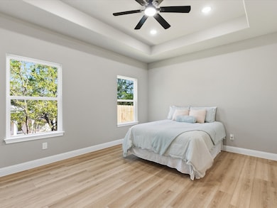 Bedroom with a raised ceiling, light wood-style floors, ceiling fan, and recessed lighting