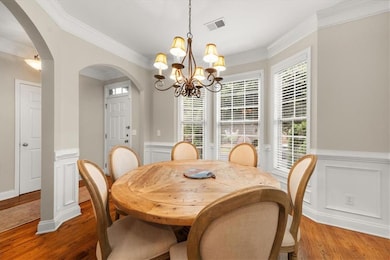 Dining room featuring arched walkways, a chandelier, light wood-style floors, ornamental molding, and wainscoting