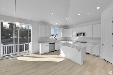 Kitchen with decorative light fixtures, light wood-type flooring, white cabinetry, a kitchen island, and plenty of natural light
