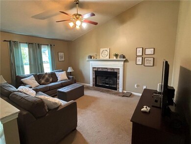 Living room with lofted ceiling, a stone fireplace, ceiling fan, and carpet