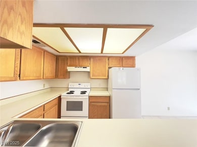 Kitchen featuring white appliances, light countertops, under cabinet range hood, and brown cabinetry