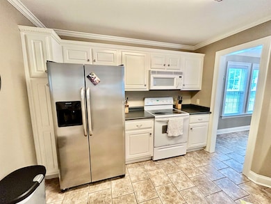 Kitchen featuring white appliances, dark countertops, crown molding, white cabinetry, and baseboards