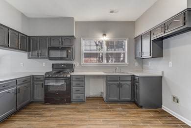 Kitchen featuring black appliances, wood tiled floors, gray cabinetry, and light countertops