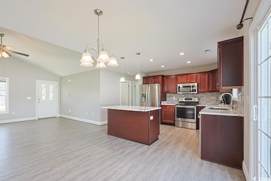Kitchen featuring appliances with stainless steel finishes, hanging light fixtures, a center island, decorative backsplash, and light wood-style floors