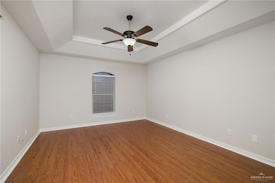 Spare room with ceiling fan, a tray ceiling, and hardwood / wood-style floors